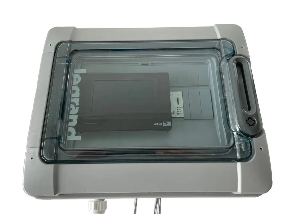 Schwarze Steuerungseinheit von Daikin, montiert in einem transparenten Gehäuse. Verschiedene Anschlüsse und Tasten sind sichtbar, mit einer klaren Abdeckung für Schutz.